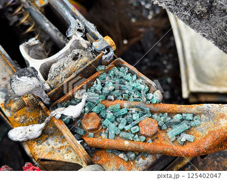 Close-up of shattered automotive safety glass scattered over a burned and rusted metal car seat frame, with visible melted elements and fire damage 125402047