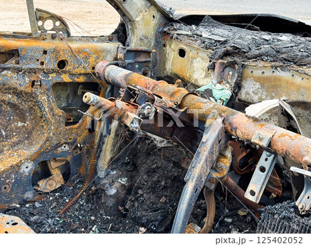 Burned steering column and dashboard frame from a car showing rusted metal structure, melted components, and complete fire destruction of the interior 125402052