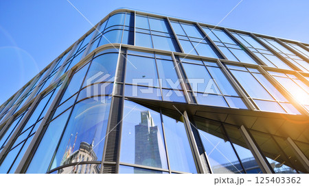 Modern office building with glass facade on a clear sky background. Transparent glass wall of office building. Modern office building with glass facade on a clear sky background. Transparent glass wall of office building. 125403362