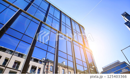 Modern office building with glass facade on a clear sky background. Transparent glass wall of office building. Modern office building with glass facade on a clear sky background. Transparent glass wall of office building. 125403366