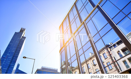 Modern office building with glass facade on a clear sky background. Transparent glass wall of office building. Modern office building with glass facade on a clear sky background. Transparent glass wall of office building. 125403368