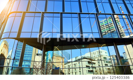 Modern office building with glass facade on a clear sky background. Transparent glass wall of office building. Modern office building with glass facade on a clear sky background. Transparent glass wall of office building. 125403386