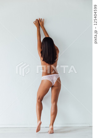 Brunette in lingerie stands with her back to a white wall 125404599