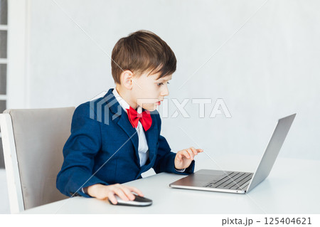 Boy in business suit at desk with laptop 125404621