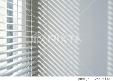 Sunlight casting striped shadows through white window blinds onto a clean wall Sunlight casting striped shadows through white window blinds onto a clean wall 125405138