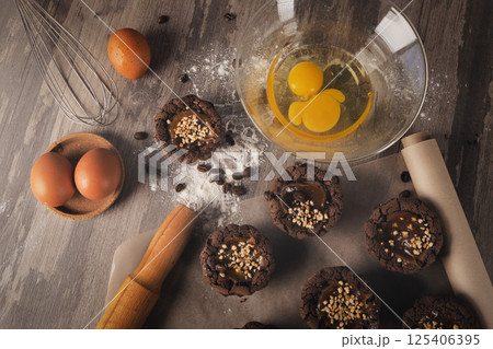 Dark brown muffins, eggs, rolling pin, bowl with breaking eggs, whisk, flour and coffee beans on a table, top view. Dark brown muffins, eggs, rolling pin, bowl with breaking eggs, whisk, flour and coffee beans on a table, top view. 125406395
