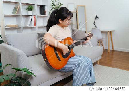 Happy Asian women play acoustic guitar and singing on the sofa in living room at home Happy Asian women play acoustic guitar and singing on the sofa in living room at home 125406872