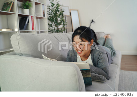 Asian young woman with glasses reading a book on the sofa in the living room happily 125406938