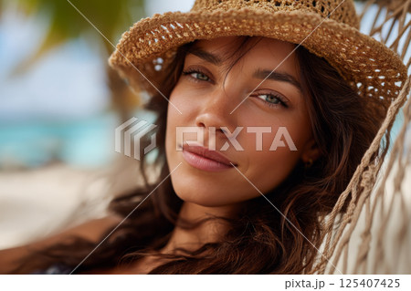 beautiful woman wearing a hat lying in a hammock on a paradise beach 125407425