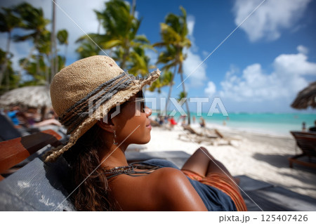 beautiful woman wearing a hat lying in a hammock on a paradise beach 125407426