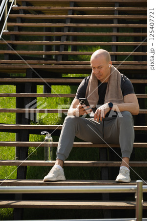 Sporty man relax, sitting on stairs using phone and texting social media after training. Summer healthy leisure activity. Outdoors. Sporty man relax, sitting on stairs using phone and texting social media after training. Summer healthy leisure activity. Outdoors. 125407721