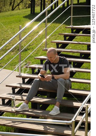 Sporty man relax, sitting on stairs using phone and texting social media after training. Summer outdoors activity 125407722