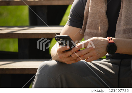 Smartphone in hands sporty man after workout. Man sitting on stairs using phone and texting social media after training. Close up. 125407726