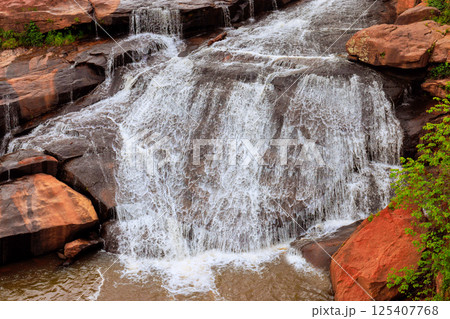 Fresh waterfall flows over rocky surface, creating serene atmosphere surrounded by greenery rugged terrain. 125407768