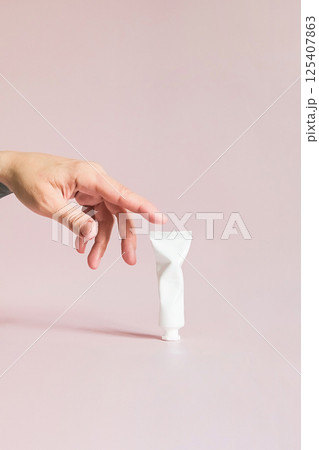 Females Hand Reaches Towards Small Crumpled White Cosmetic Product Tube. Beauty Treatment Concept. 125407863