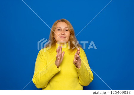 Caucasian woman in her 40s feeling happy and successful, smiling and clapping, saying congratulations with a handclap against a blue wall. 125409038