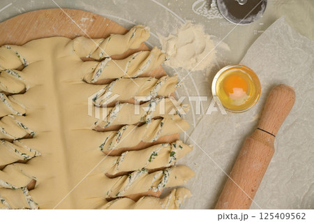 Top view close up twisted dough strips on wooden board. Cutter, egg, rolling pin on kitchen table. Home cooking baking puffs Top view close up twisted dough strips on wooden board. Cutter, egg, rolling pin on kitchen table. Home cooking baking puffs 125409562