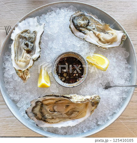 Open oysters on a vintage vintage dish with slices of crushed ice and half a lemon closeup on a black stone textured background. Right angle view from above. Aphrodisiac. 125410105