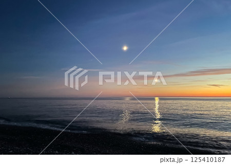 moon and the light of an airplane at night over the sea at sunset. Two moon trails on the water. moon and the light of an airplane at night over the sea at sunset. Two moon trails on the water. 125410187
