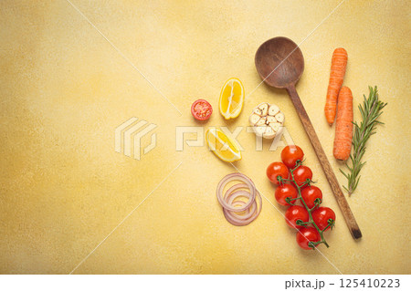 Cooking ingredients, fresh vegetables and wooden spoon on yellow background with copy space, cooking background 125410223