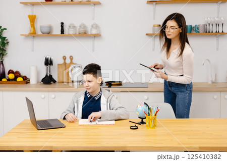 A young woman helps a boy with his lessons using a tablet and a globe. A homeschooling student does his homework with the help of a tutor 125410382