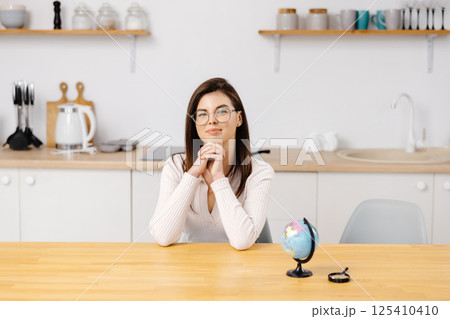 Caucasian student girl smiles, looking to camera and studies geography on a globe while sitting at home in quarantine. Education abroad. Distance learning 125410410