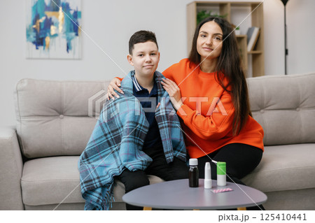 A young mother and her son are sitting on the sofa at home. A mother is treating her son for a viral infection at home A young mother and her son are sitting on the sofa at home. A mother is treating her son for a viral infection at home 125410441