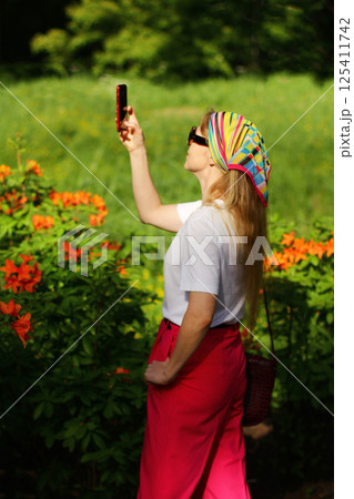 A girl takes pictures of flowers in the garden in summer on her phone. Travel blogger photographs nature, selective focus 125411742