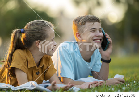 Happy teenagers talking on cellphone outdoors sitting in summer park Happy teenagers talking on cellphone outdoors sitting in summer park 125413379