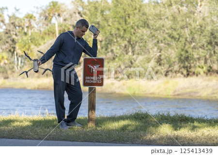 Drone operator is disappointed because he isn't allowed to fly his quadcopter in national park no drone area. Man is unable to use his UAV near restriction notice sign. Airspace use regulations Drone operator is disappointed because he isn't allowed to fly his quadcopter in national park no drone area. Man is unable to use his UAV near restriction notice sign. Airspace use regulations 125413439