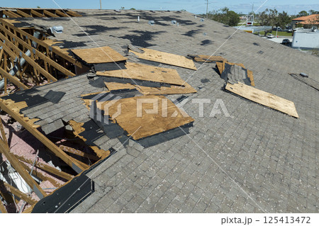 Damaged house roof with missing shingles after hurricane Ian in Florida. Consequences of natural disaster Damaged house roof with missing shingles after hurricane Ian in Florida. Consequences of natural disaster 125413472
