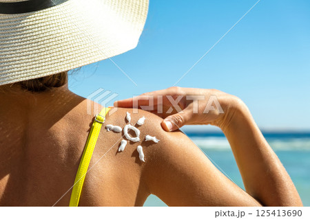 Back view of young woman tanning at the beach with sunscreen cream in sun shape on her shoulder. UV sunburn protection and sunblock skincare concept Back view of young woman tanning at the beach with sunscreen cream in sun shape on her shoulder. UV sunburn protection and sunblock skincare concept 125413690