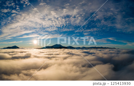 Aerial view of vibrant sunrise over white dense fog with distant dark Carpathian mountains on horizon. Aerial view of vibrant sunrise over white dense fog with distant dark Carpathian mountains on horizon. 125413930