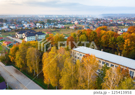 Aerial view of school, college or kindergarten building with big yard among autumn trees on rural landscape background Aerial view of school, college or kindergarten building with big yard among autumn trees on rural landscape background 125413958