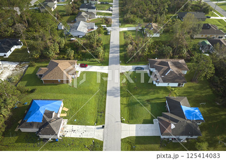 Aerial view of damaged in hurricane Ian houses roofs covered with blue protective tarp against rain water leaking until replacement of asphalt shingles 125414083