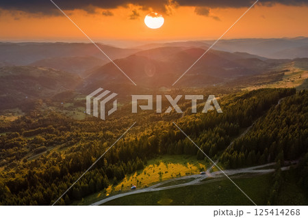 Aerial view of colorful sunset in wild mountains. Dark dirt road winding through pine forest illuminated with bright setting sun. Beautiful nature landscape Aerial view of colorful sunset in wild mountains. Dark dirt road winding through pine forest illuminated with bright setting sun. Beautiful nature landscape 125414268