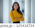 A woman in a yellow shirt and black skirt stands by a window 125414724