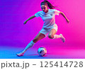 A young woman is kicking a soccer ball on a colorful background 125414728