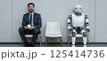 A man in a suit sits next to a robot, talking or observing it 125414736