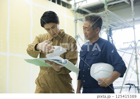現場で図面を見ながら打ち合わせする現場監督 現場で図面を見ながら打ち合わせする現場監督 125415389