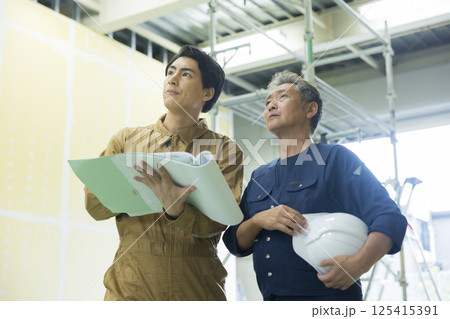 現場で図面を見ながら打ち合わせする現場監督 125415391