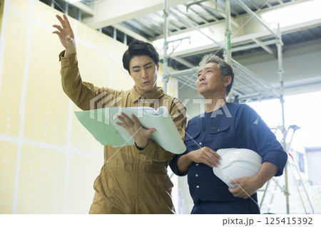 現場で図面を見ながら打ち合わせする現場監督 現場で図面を見ながら打ち合わせする現場監督 125415392