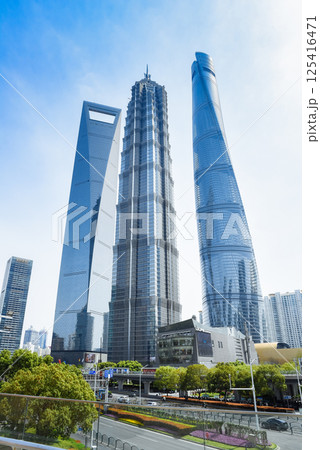 Shanghai, China - 1 April 2025: Lujiazui's iconic skyline: Shanghai Tower, Jin Mao Tower, and Shanghai World Financial Center, framed by greenery and urban infrastructure under blue skies 125416471