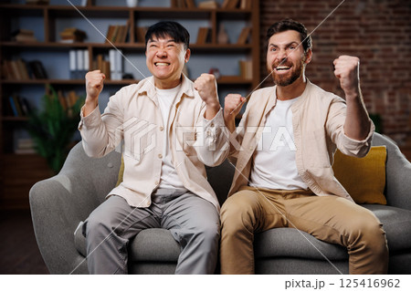 fans watching game, celebrating victory, Excited friends watching TV, Friends express their enthusiasm and joy while watching a sports event from a comfortable couch in a cozy living room. Their 125416962
