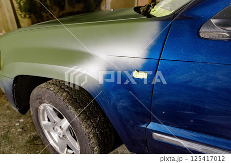 Vehicle shows a combination of primer and painted areas on its front fender while being worked on in a garage. The contrast highlights the preparation process for a full repaint. 125417012