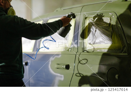 A technician sprays paint onto a car with precise control in a well-equipped garage. The atmosphere shows a focus on quality and craftsmanship during the restoration work. A technician sprays paint onto a car with precise control in a well-equipped garage. The atmosphere shows a focus on quality and craftsmanship during the restoration work. 125417014