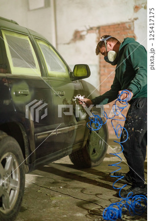 A car painter works diligently in a workshop, using a spray gun to apply paint to a vehicle. The workspace is filled with tools, highlighting the process of automotive refinishing. A car painter works diligently in a workshop, using a spray gun to apply paint to a vehicle. The workspace is filled with tools, highlighting the process of automotive refinishing. 125417175