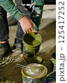 A person is holding a paint can, pouring vibrant green paint as they prepare for a creative endeavor in a dimly lit workshop. Various other paint cans are scattered around. 125417252