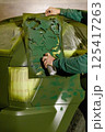 A person applies a green camouflage design on a vehicle using a spray can and a stencil. The workshop setting shows preparations for painting, highlighting creativity and craftsmanship. 125417263