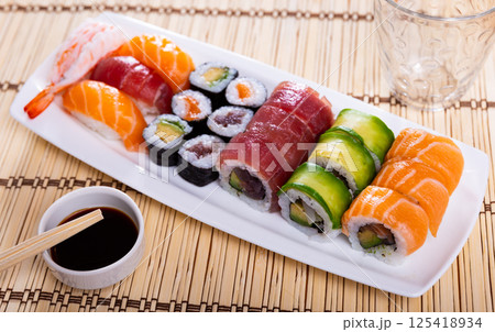 On table there is white narrow rectangular plate with set with maki - uramaki and nigiri 125418934